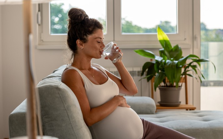pregnant woman drinking water on couch