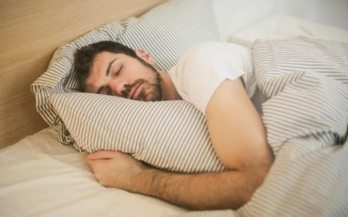 Man lying in bed asleep with arm under pillow.