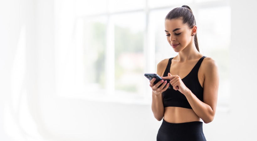 Young woman in black sports gear using a fitness app on a smartphone.