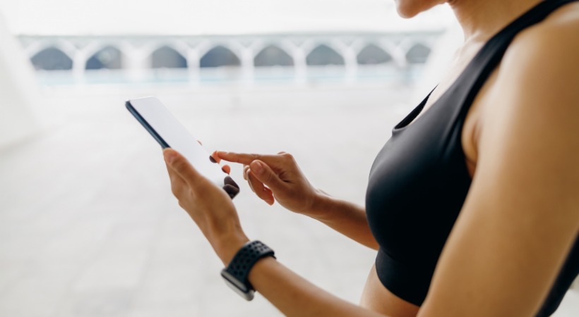 Close up of woman in black sports gear using a fitness app on a smartphone.