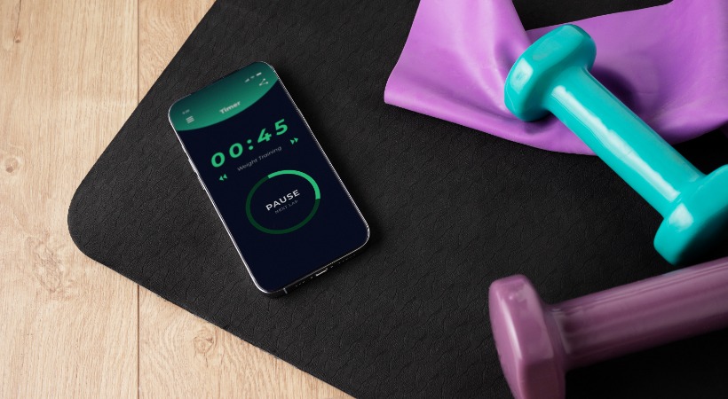 Smartphone displaying generic fitness app on a yoga mat next to multi-coloured dumbells.